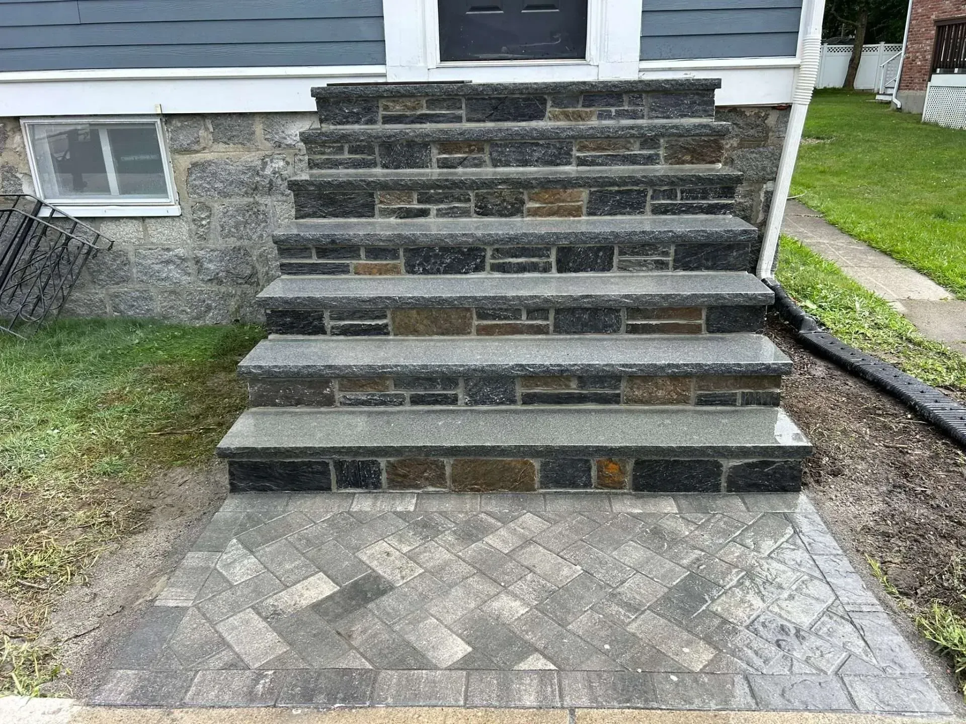 Stone steps leading up to a blue house with brick detailing and a patterned walkway.