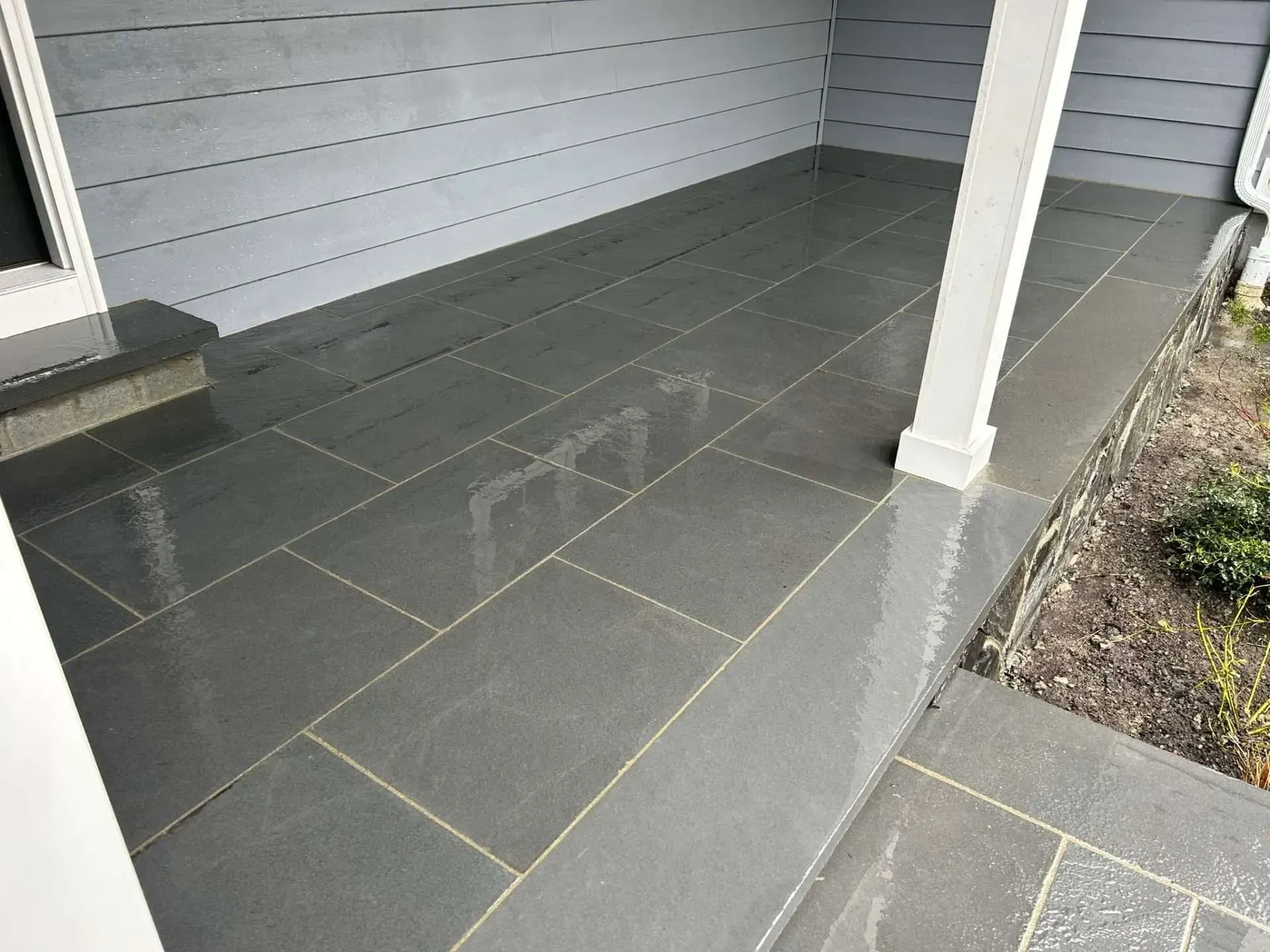 Gray tiled front porch with a white pillar and gray siding.