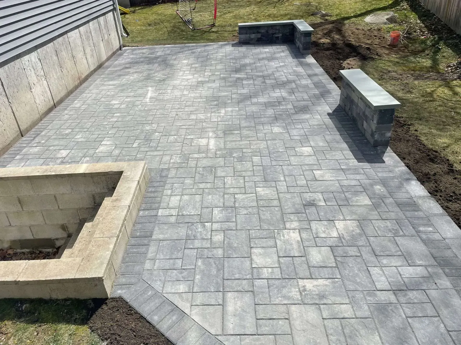 Stone patio with retaining walls next to a building and grass.