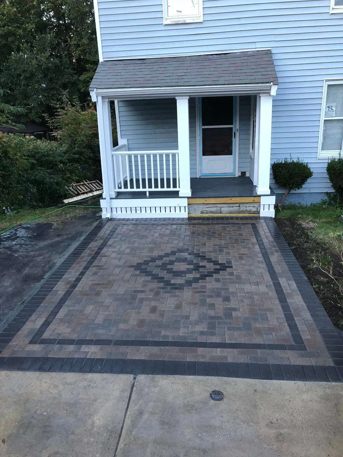 Paver patio with a decorative center pattern, in front of a blue house with a white porch.