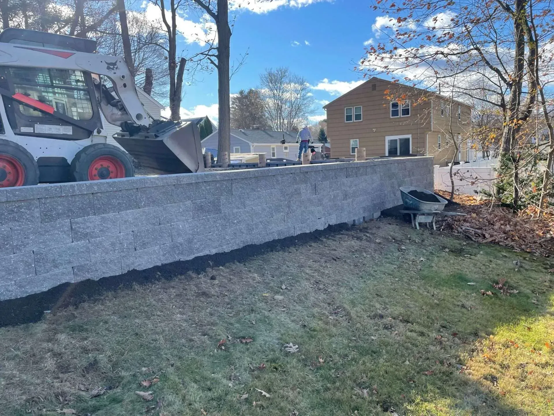 Bobcat machine constructing a retaining wall near a house on a sunny day.