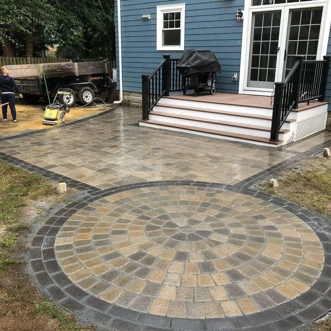 Newly constructed brick patio with circular design and steps leading to a blue house.