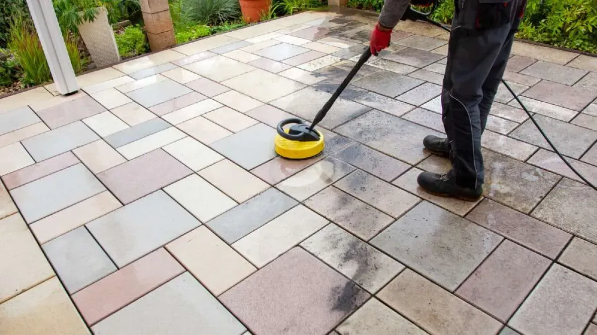 Person pressure washing a multi-colored patio.
