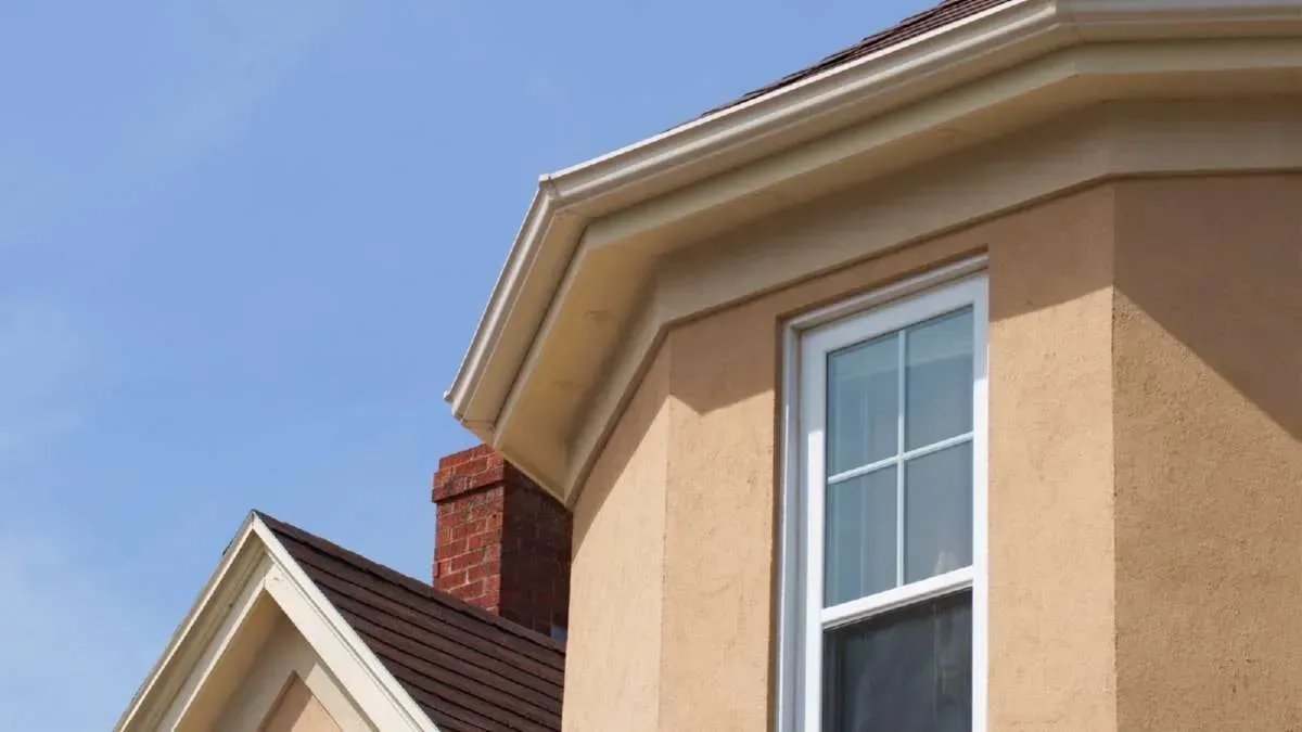 Tan stucco house exterior with white window, red brick chimney, and blue sky.