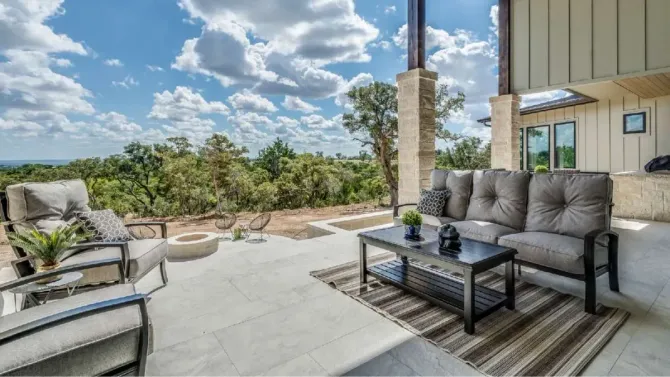 Patio with outdoor furniture, overlooking trees and a cloudy sky.