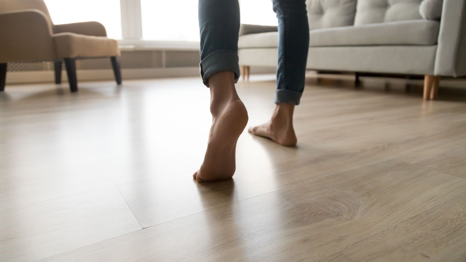 A woman is walking barefoot on a wooden floor in a living room.