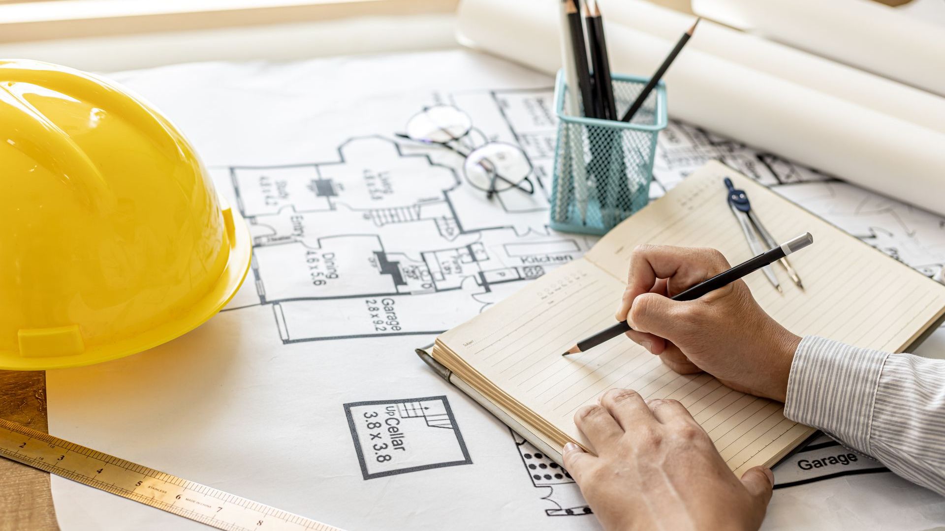 A man is writing in a notebook next to a hard hat.