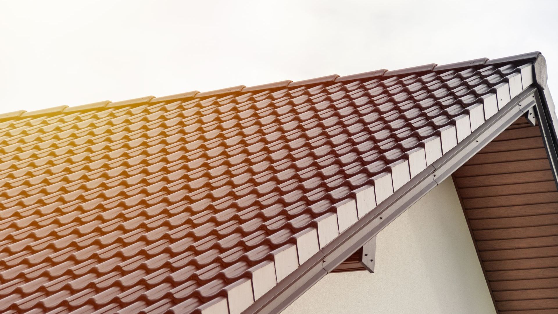 The roof of a house with a brown tile roof and a white gutter.