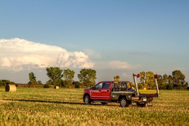 Red pickup truck in a field with farm equipment under a blue sky at sunset