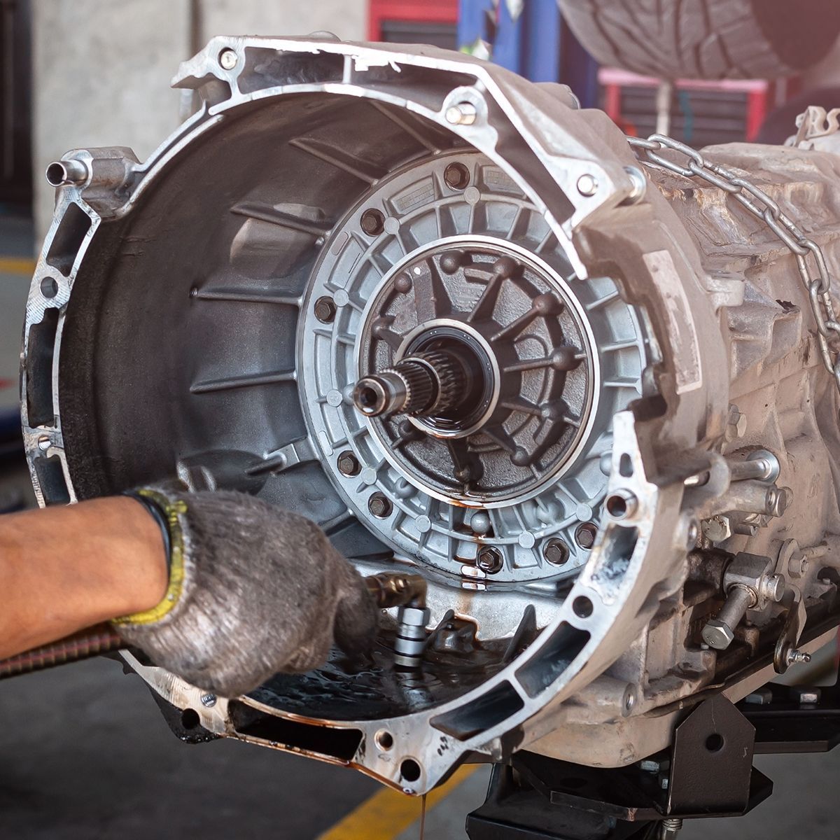 A man is working on a car transmission in a garage.