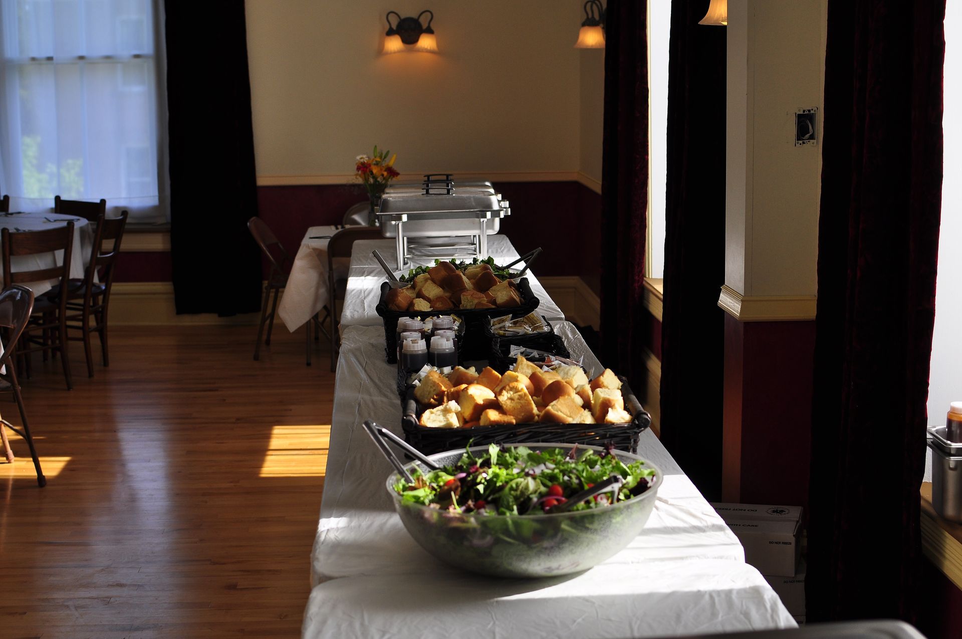 Buffet table with various dishes in a brightly lit room with a wood floor and tables.