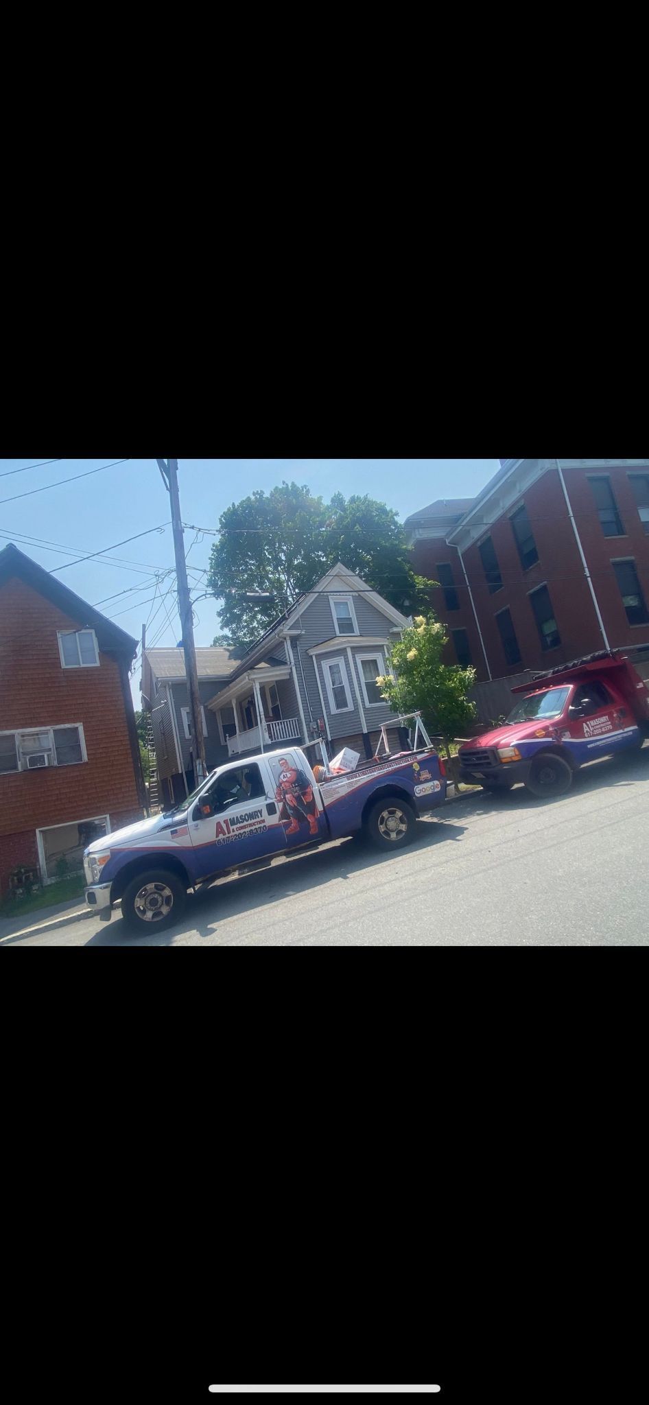 Tow trucks parked on a city street, one red and one purple and white. Buildings line the street.