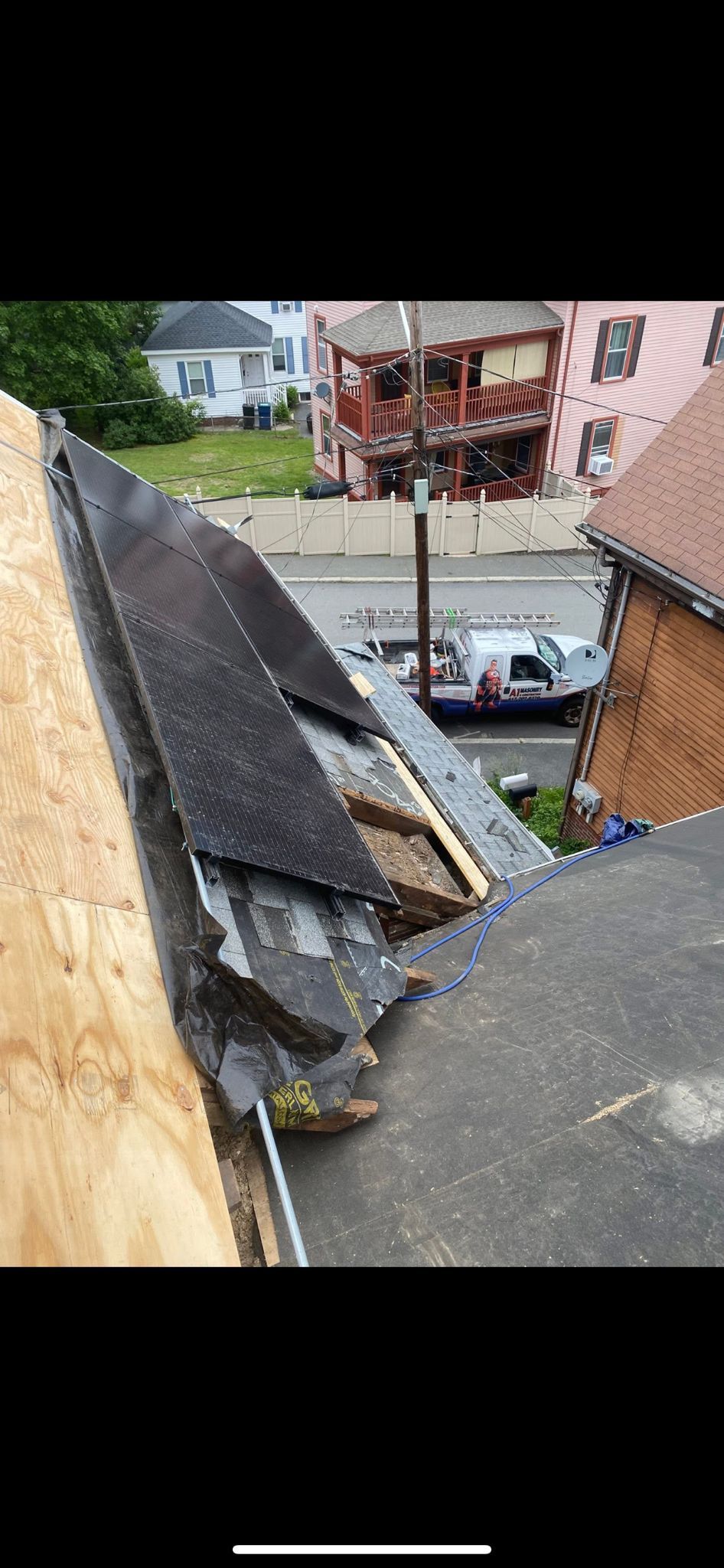 Damaged roof with missing shingles, revealing wood. Exterior view with other buildings.