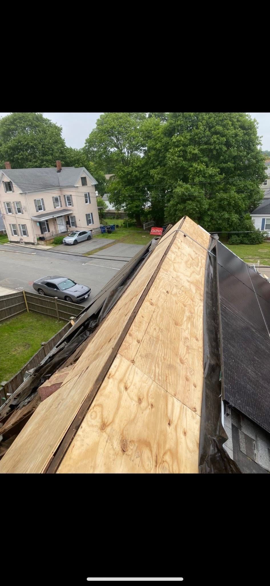 A partially constructed roof, with new wood planks, overlooking a neighborhood with trees and houses.