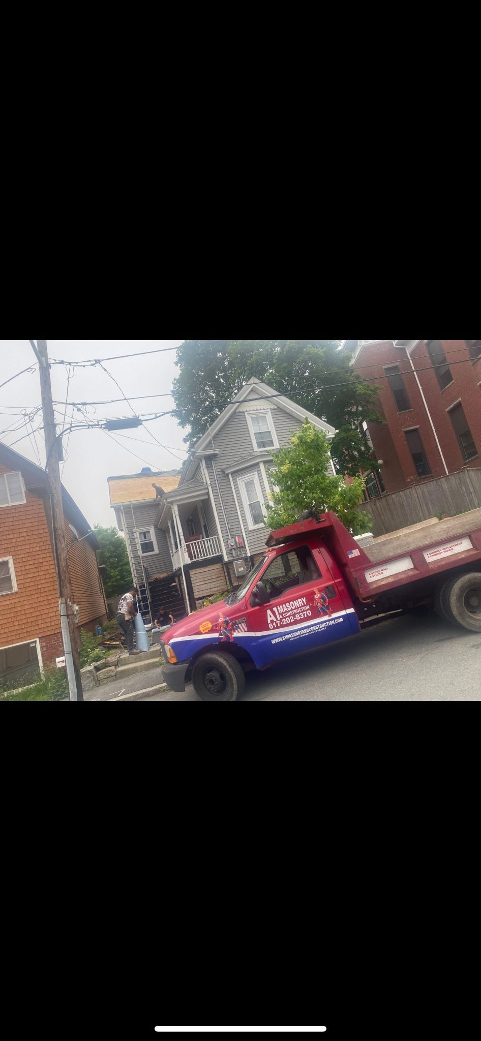 A red and blue work truck parked on a street near a house and a brown building.