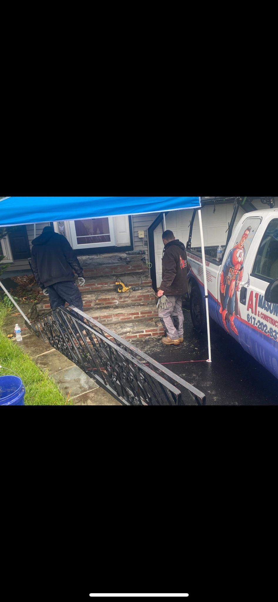 Two people near a van, in a wet outdoor setting, under a blue tarp.