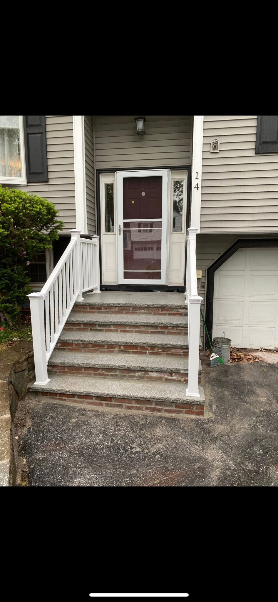 Front view of a house with steps leading to the front door. White railing on the stairs. Gray siding on the house.