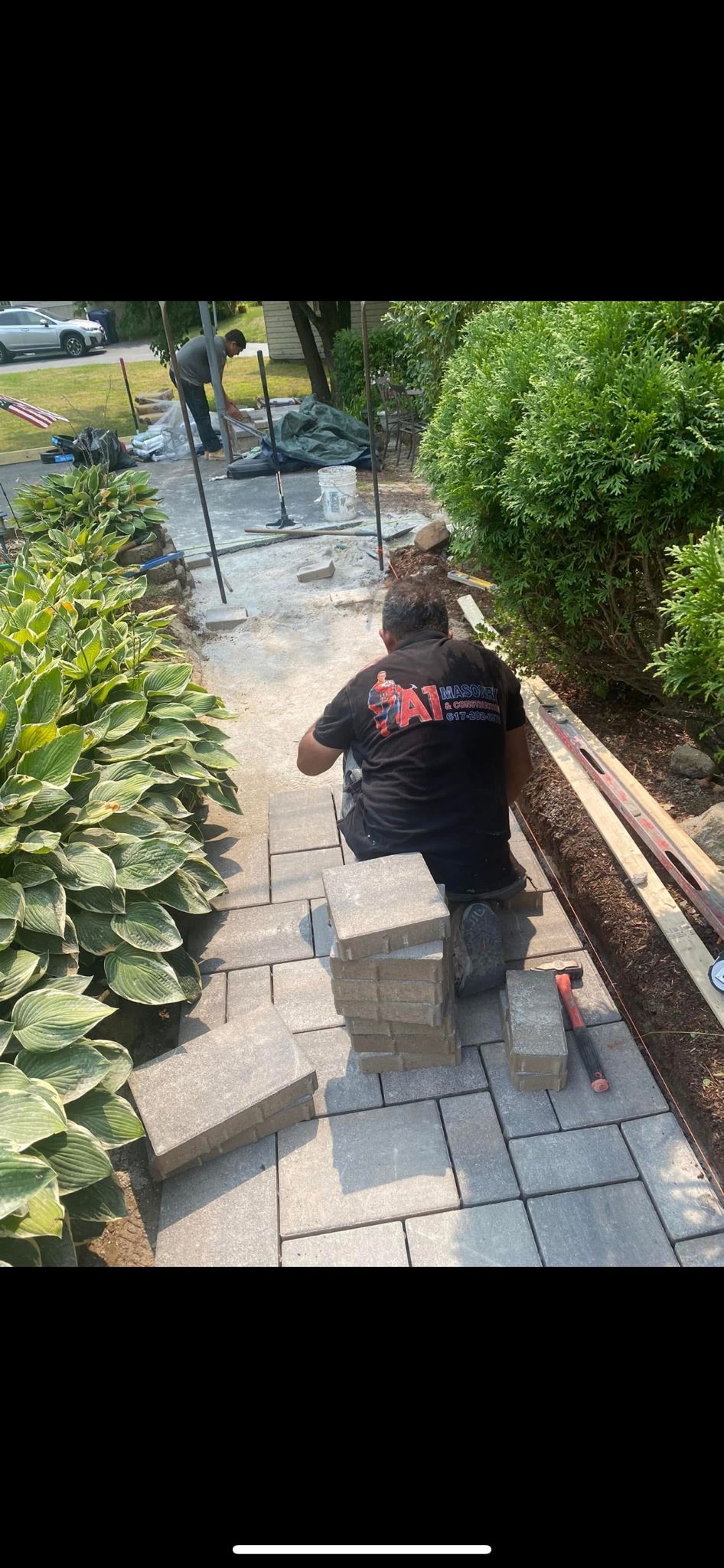 Man laying paving stones on a pathway lined with bushes and foliage.