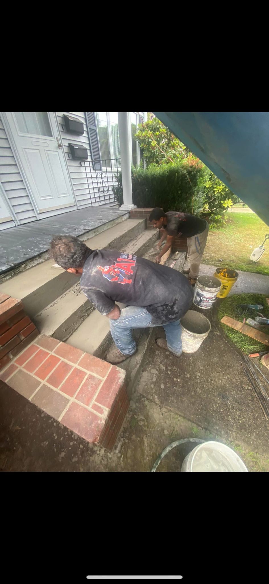 A person is crouching and working on brick steps in front of a house.