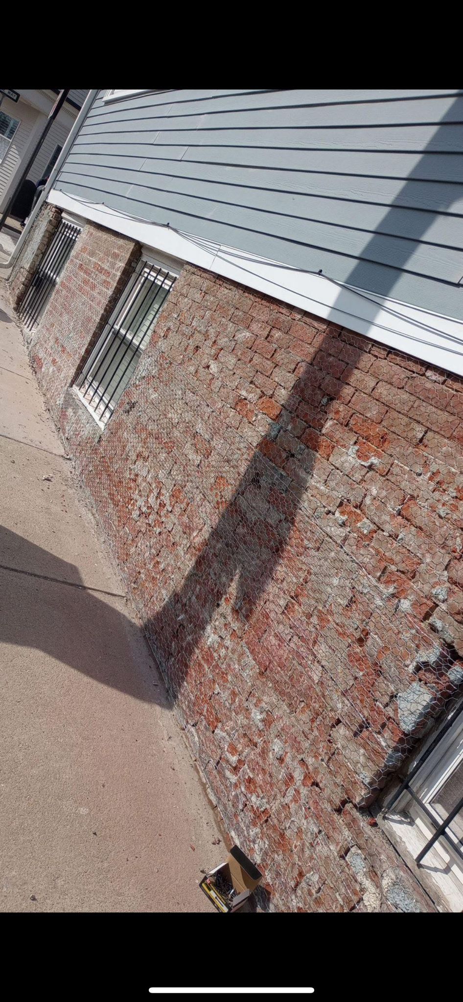 Brick building exterior with gray roof and a shadow cast on the ground.