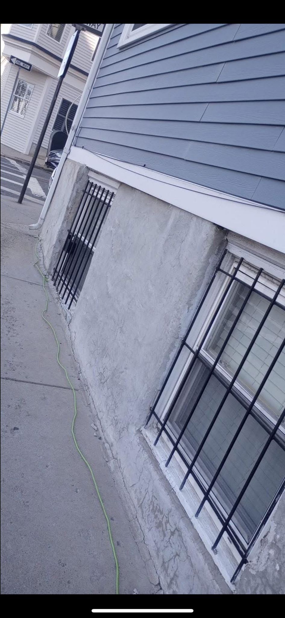 Exterior of a building with blue siding and barred windows. A sidewalk runs alongside it.