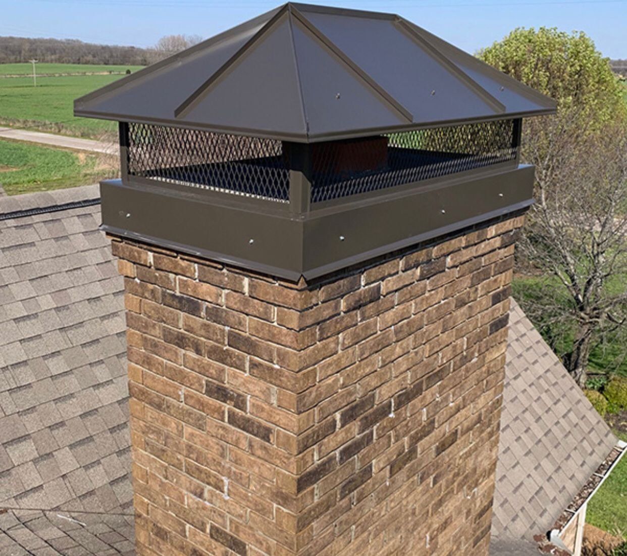 Brick chimney with a dark brown metal cap and mesh screen.