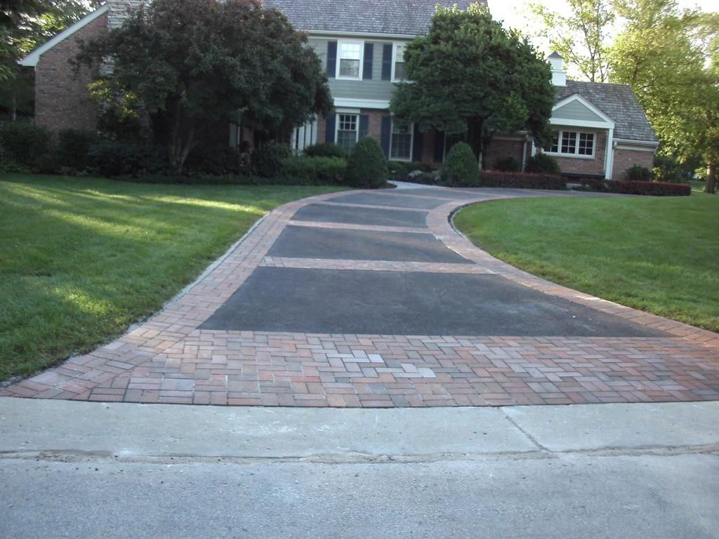 Brick-bordered driveway leading to a two-story house with a green lawn.