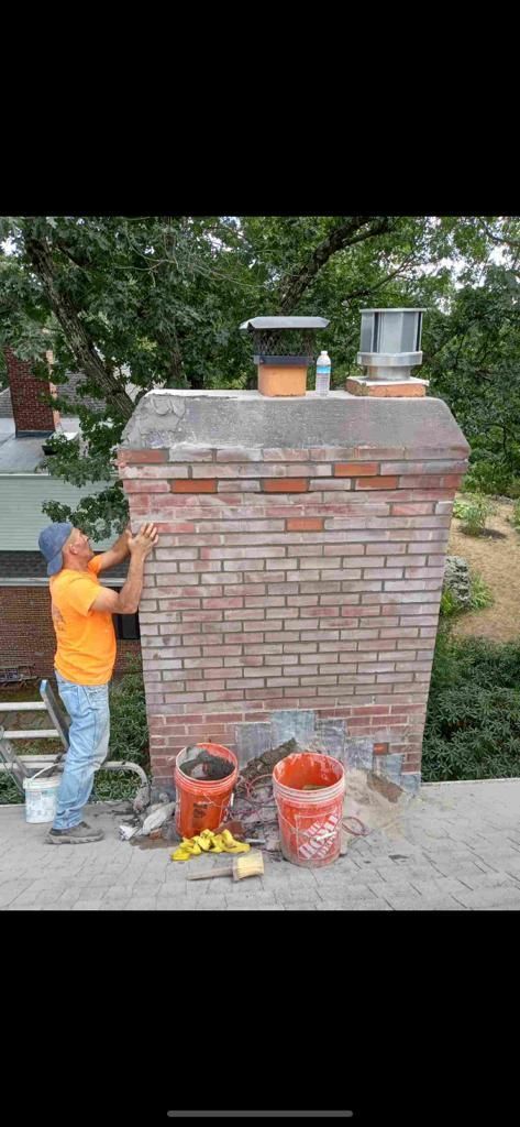 Person repairing a brick chimney on a rooftop, using tools from orange buckets.