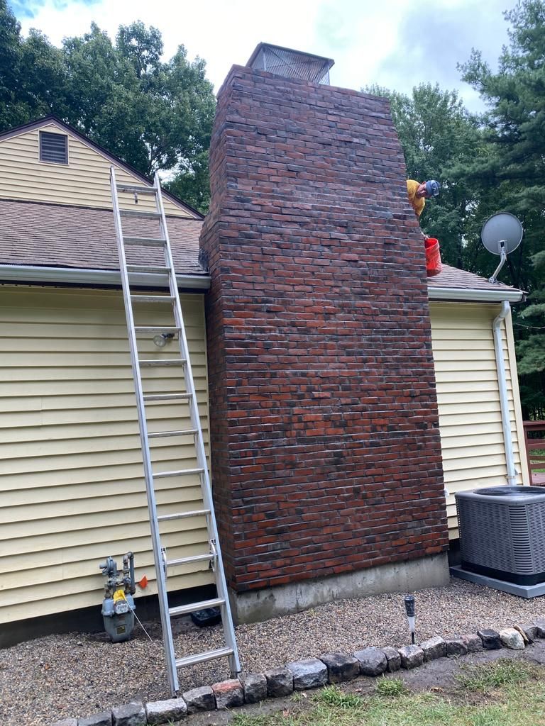 Ladder against a yellow house leading to a brick chimney; someone on the roof.