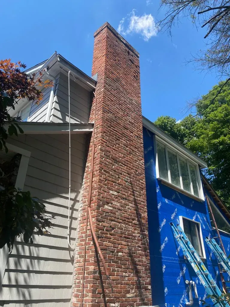 Brick chimney on a blue house with white trim against a bright sky.