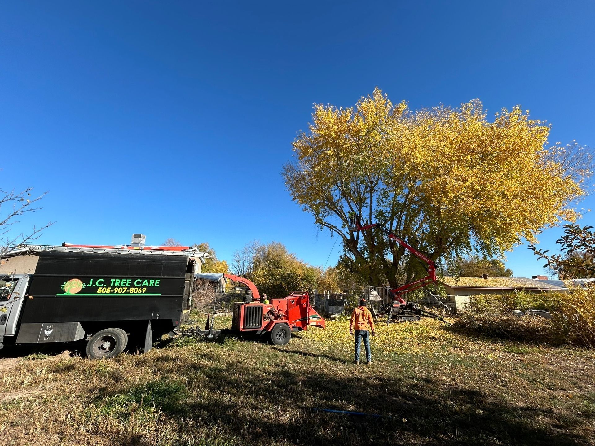 Worker beside red excavator near black truck in a grassy field under a bright blue sky