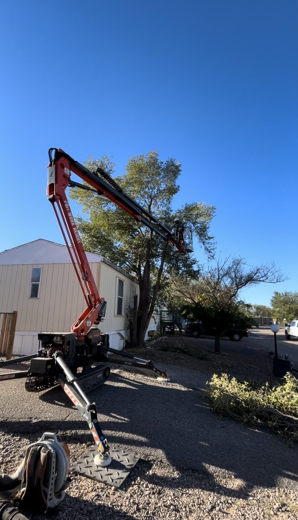 A tree trimming machine with a raised arm, next to a house under a blue sky.