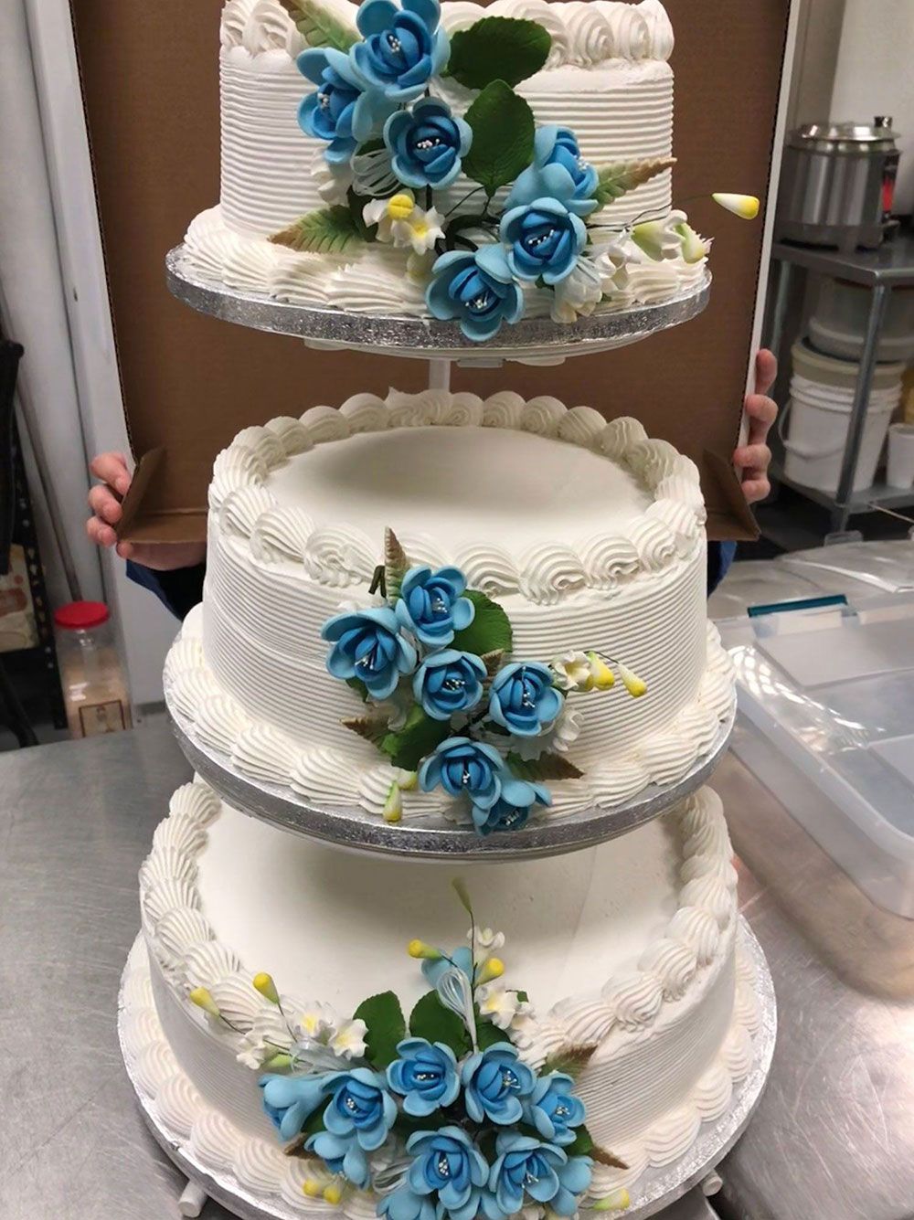 A three tiered wedding cake with blue roses on it is sitting on a table.