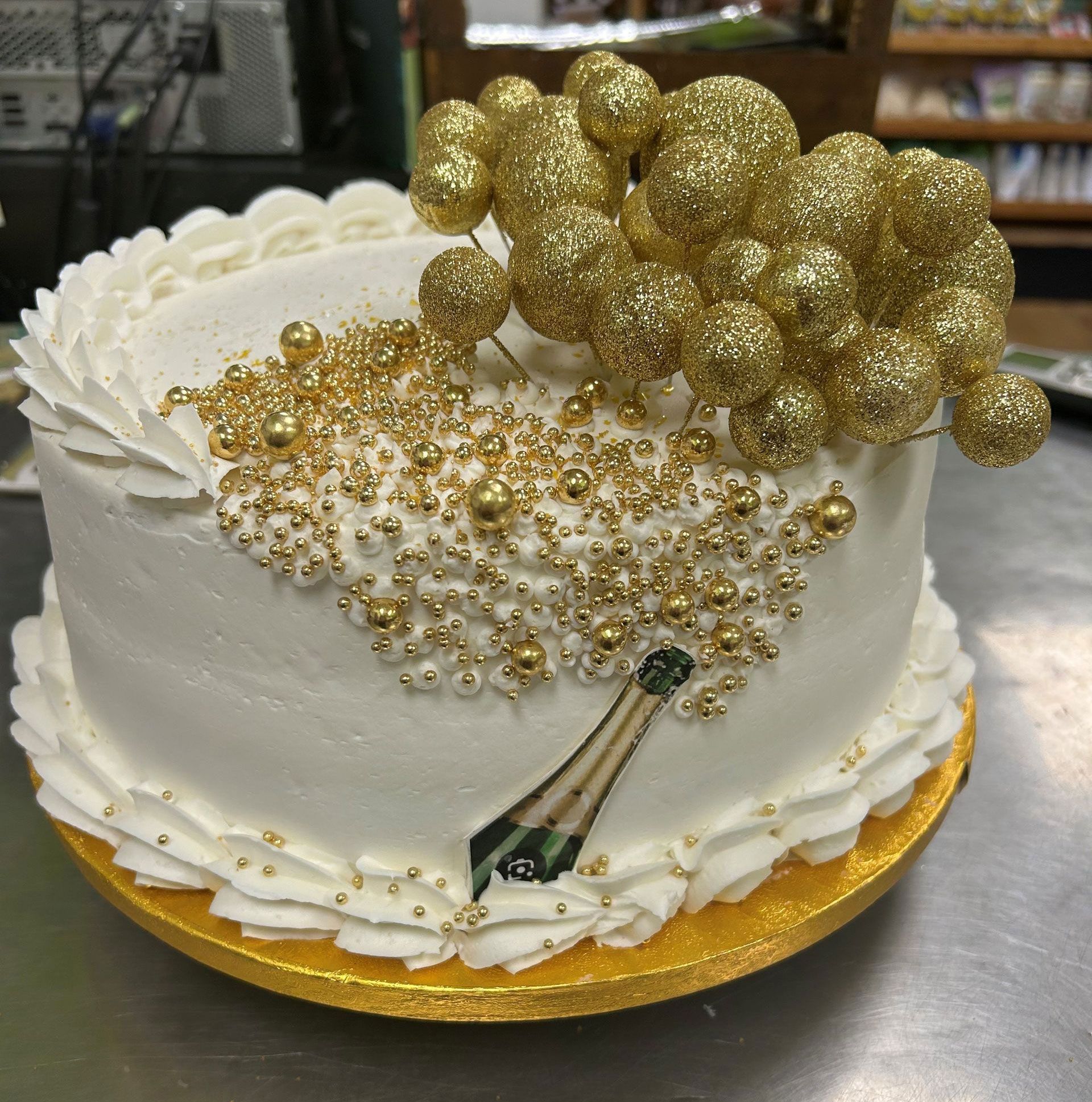 A white cake with gold sprinkles and a bottle of champagne on it