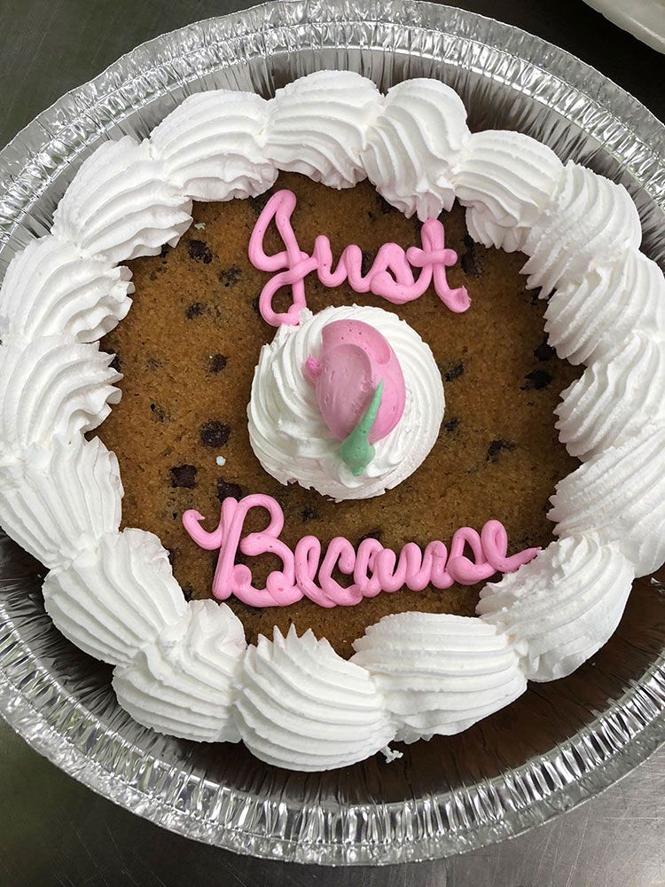 A cookie cake with whipped cream and pink writing that says just because