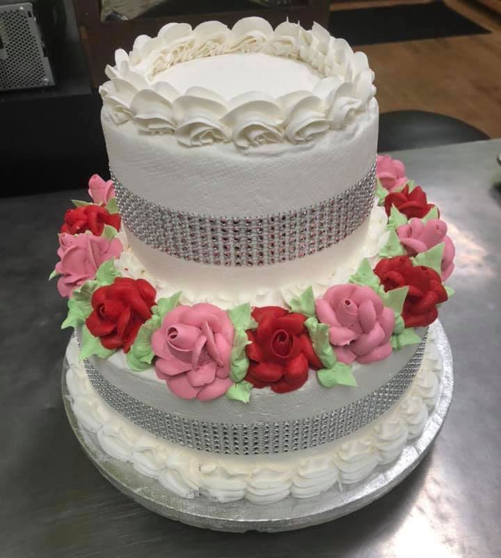 A three tiered cake with pink and red roses and rhinestones
