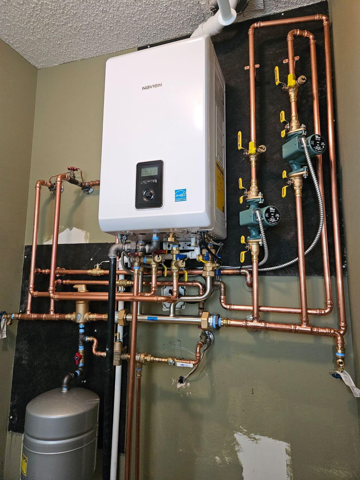 A white water heater is mounted to a wall surrounded by copper pipes.