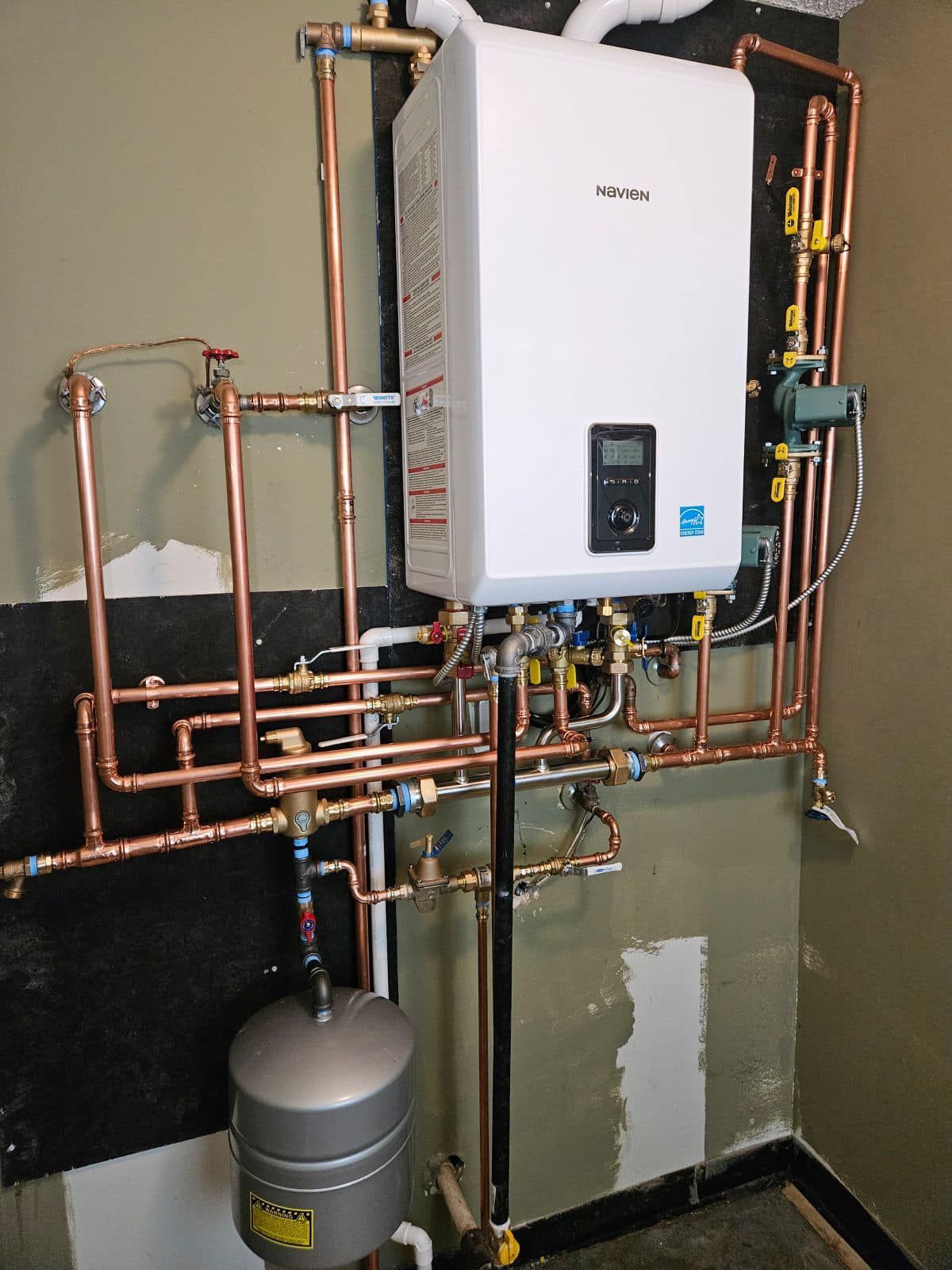 A white water heater is surrounded by copper pipes.