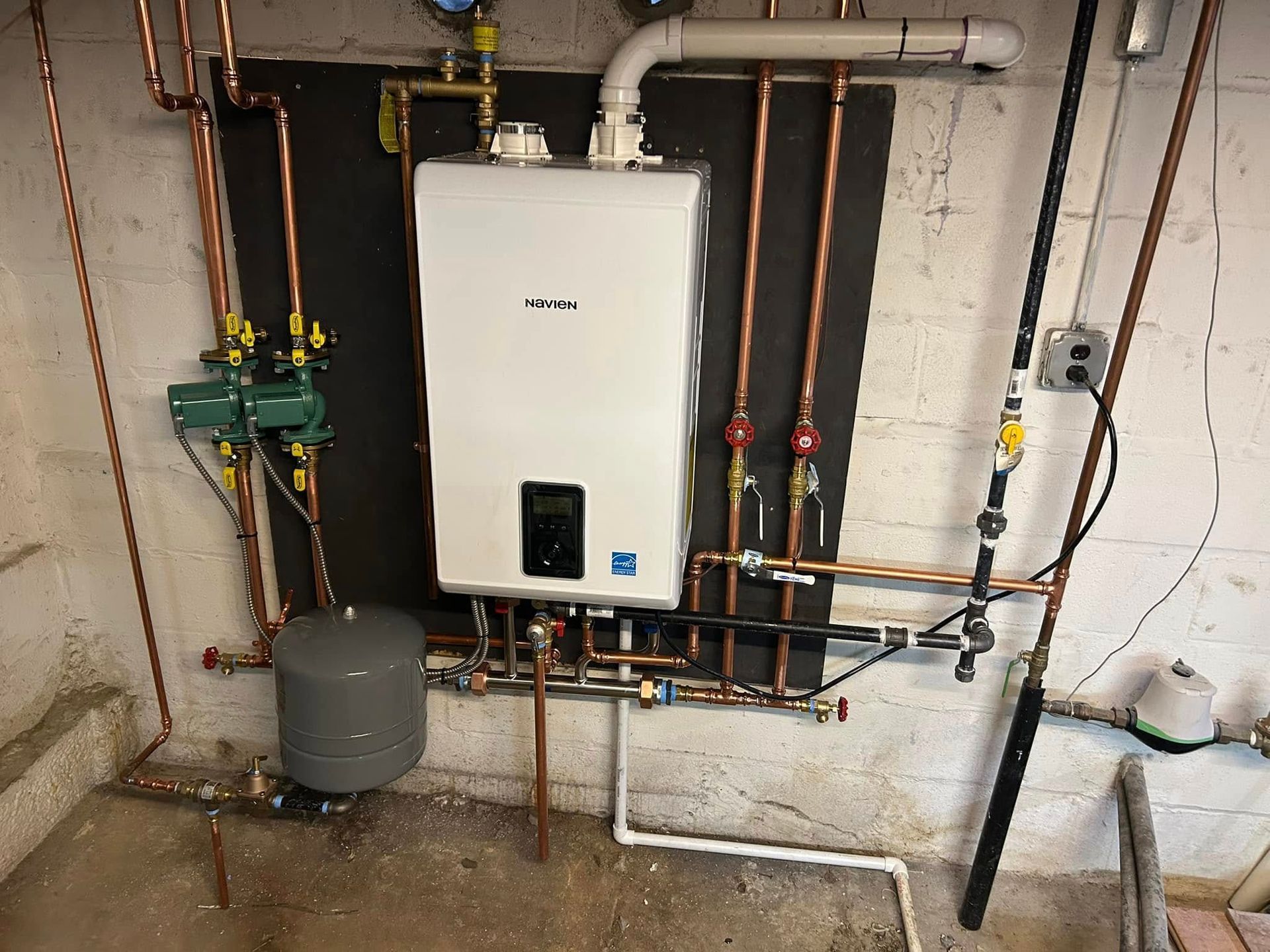A white water heater is hanging on a wall next to copper pipes.