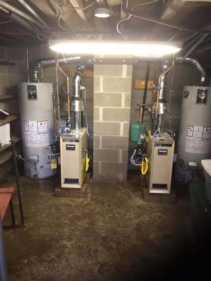 Two water heaters are sitting next to each other in a basement.