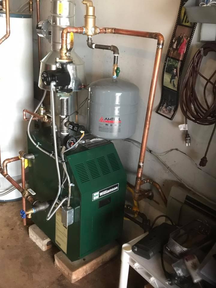A boiler is sitting in a garage next to a water heater.