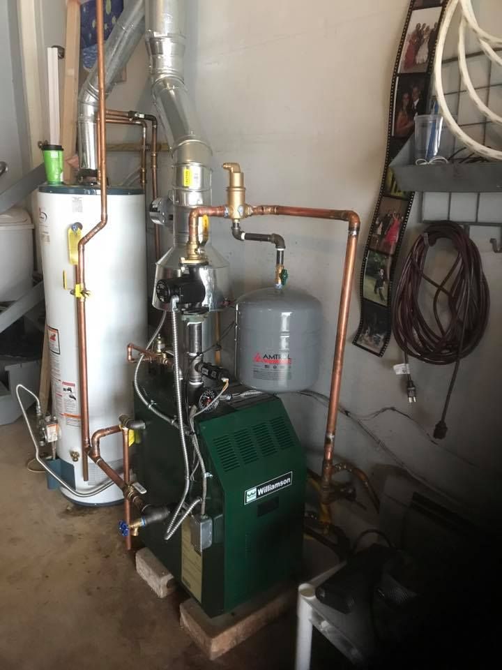 A green water heater is sitting next to a white water heater in a garage.