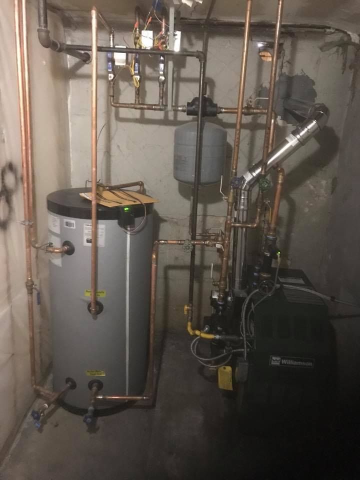 A water heater is sitting in a basement surrounded by pipes.