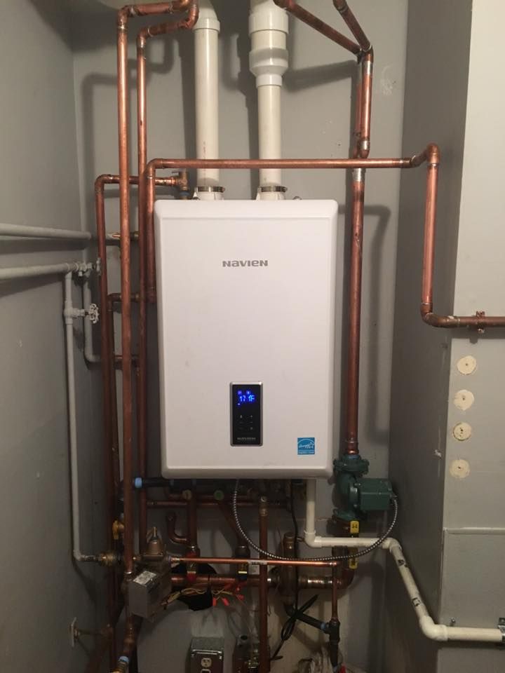 A white water heater is hanging from copper pipes in a room.