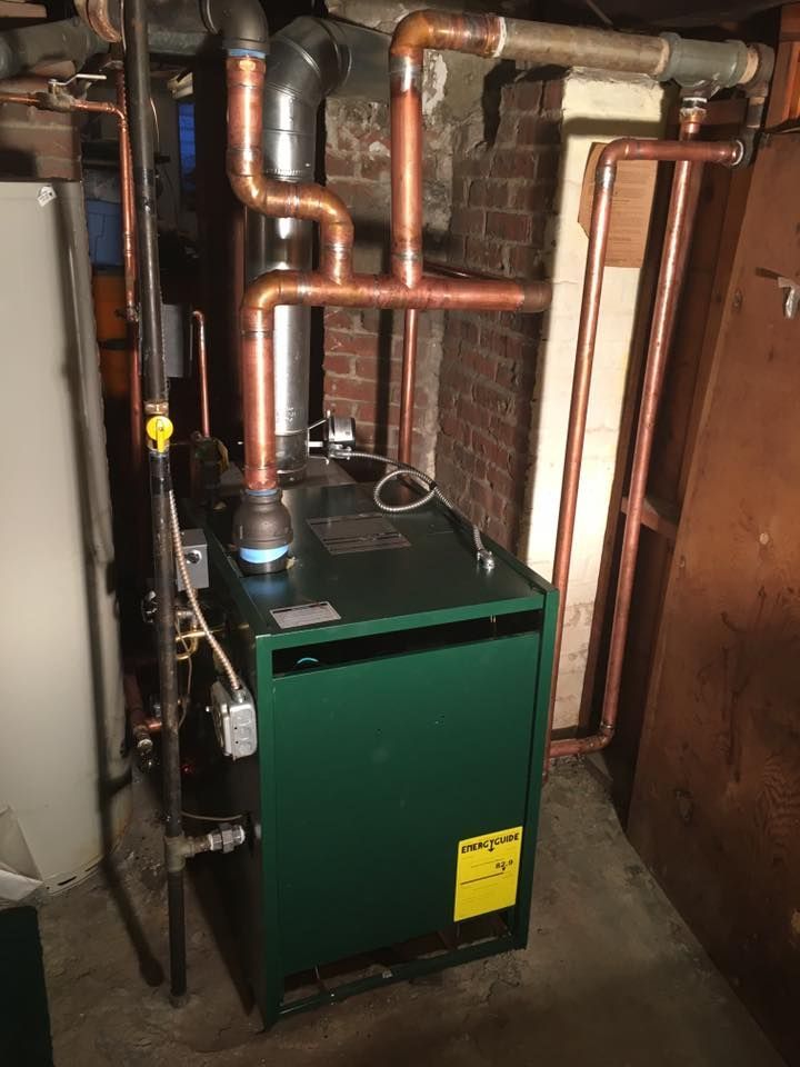 A green boiler is sitting in a basement next to a brick wall.