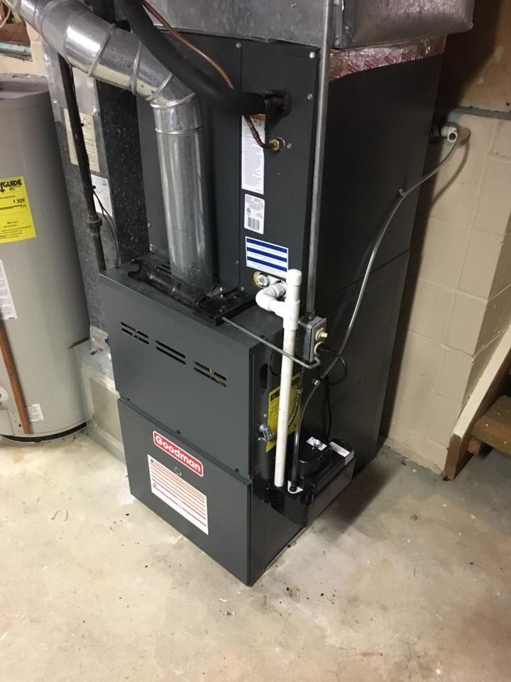 A furnace is sitting in a basement next to a water heater.