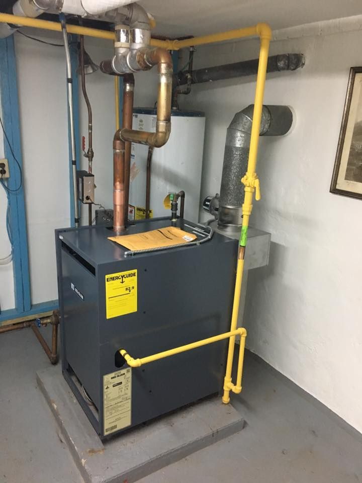 A boiler is sitting in a room with pipes and a picture on the wall.