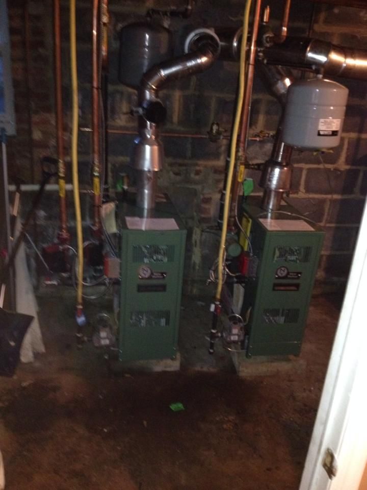 Two green boilers are sitting in a basement next to a brick wall.