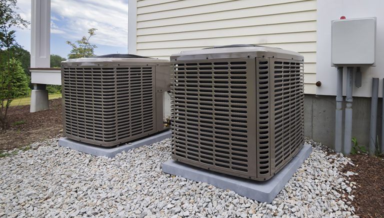 Two air conditioners are sitting outside of a house.