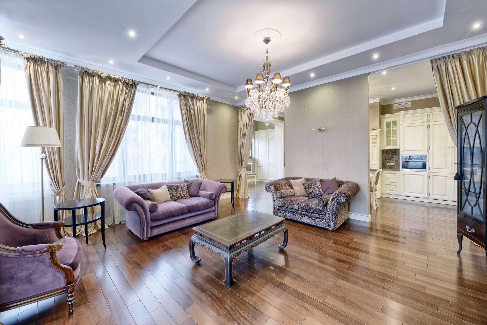 Luxurious living room with purple sofas, wood floor, and chandelier.